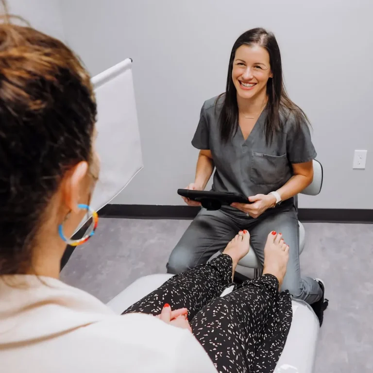 Female medical staff sitting on stool with ipad smiling at patient in chair