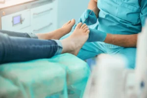 A person in scrubs is performing a foot treatment on someone's foot.