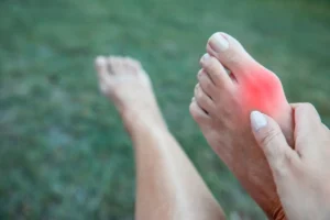 Image of a foot with a bunion highlighted in red and held by a woman's hand