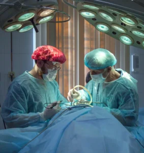 Image of two surgeons in an operating room dressed in green scrubs with a patient draped in blue lying down in the foreground and operating on a bunioni