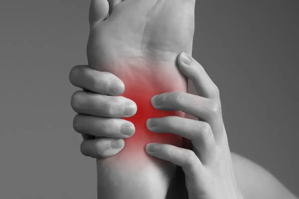 Black and white image of underside of foot, the inner arch of the foot highlighted in red, with hands holding the foot, fingers on the arch