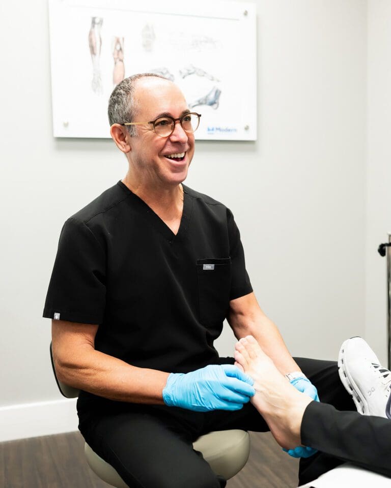 Dr. Stephen Baker, a male podiatrist wearing black scrubs, examining a patient's foot in clinic in Tampa, Florida