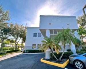 Exterior photo of a 2 story grey building with porte cochere and parkiing lot, the medical building of modern foot & ankle in Lake Worth, Florida