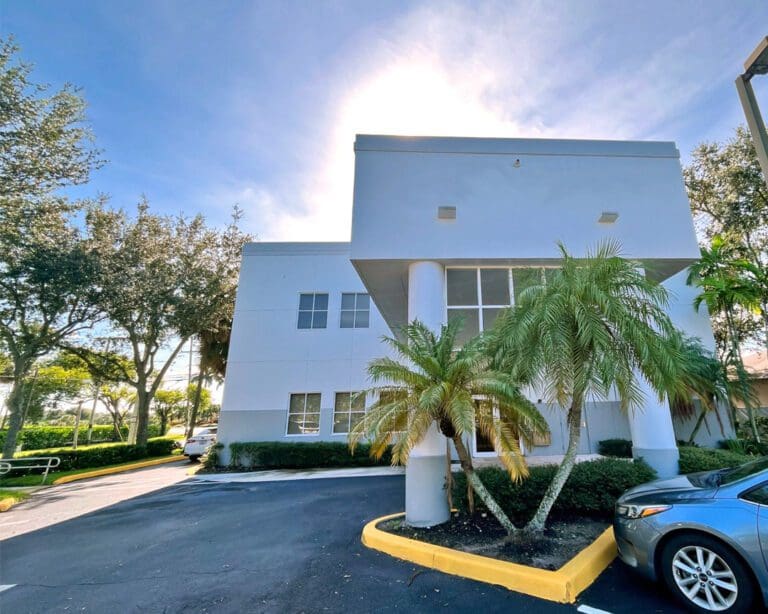 Exterior photo of a 2 story grey building with porte cochere and parkiing lot, the medical building of modern foot & ankle in Lake Worth, Florida