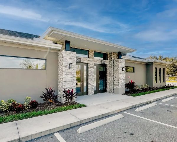 Modern Podiatrist Orlando office in Kissimmee, showcasing a beige exterior with elegant stone pillars, dark green glass doors, and a landscaped front with colorful plants.