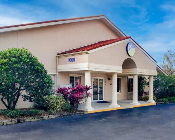 Podiatrist Orlando office in Oviedo featuring a beige one-story building with a red-tiled roof, arched entryway, the number '1000' prominently displayed, and landscaping with vibrant purple plants and green shrubs.