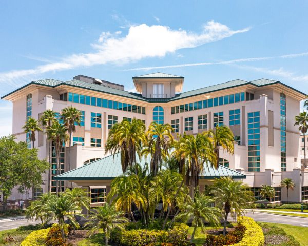 Exterior front view of the Sarasota office in Sarasota, Florida, showing a peach, mid-rise l-shaped medical building with porte cochere and surrounded by palm trees.