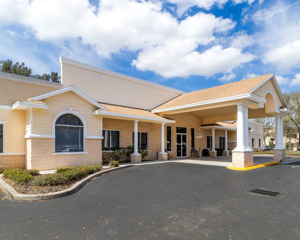 Podiatrist Tampa office situated in Brandon, presenting a warm beige complex with varied roofing styles, including arched entryways and a bay window. A well-maintained parking lot features handicapped spaces, and mature trees offer shade to the vicinity.