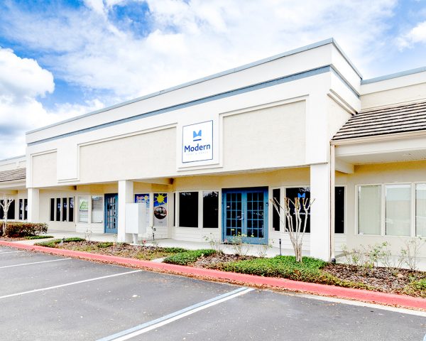 Podiatrist Orlando office in Casselberry featuring a beige building facade, vibrant blue entrance door, Modern Foot & Ankle signage, and blooming red flowers in the foreground.