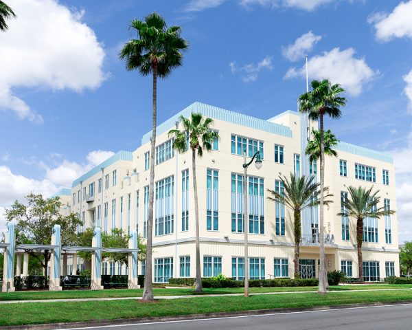 Aerial view of a large, contemporary Podiatrist Orlando office building in Celebration, with a white facade, palm trees lining the entrance, and an expansive parking area.