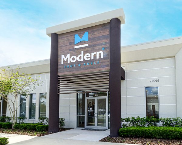 Aerial view of the spacious, modern Podiatrist Lake Nona office in Orlando, showcasing a sleek white exterior, lush palm trees at the entrance, and a large parking facility.